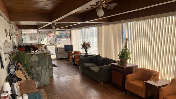A spacious living area with a wooden floor, a green sofa, and a coffee table. There is a small kitchen area with a refrigerator and a television. - Fort Collins Inn (Fort Collins)