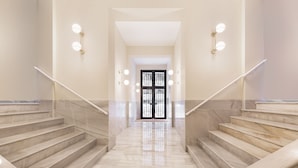 Una escalera de mármol que conduce a una puerta con un panel de vidrio, flanqueada por paredes con lámparas.
