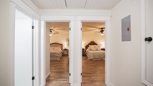 A hallway leading to two bedrooms with wooden floors, white walls, and ceiling fans. - Spacious Vacation Home: Sleeps 16, 1/2 mi to Beach & Boat Ramp - Family Friendly (Port O'Connor)