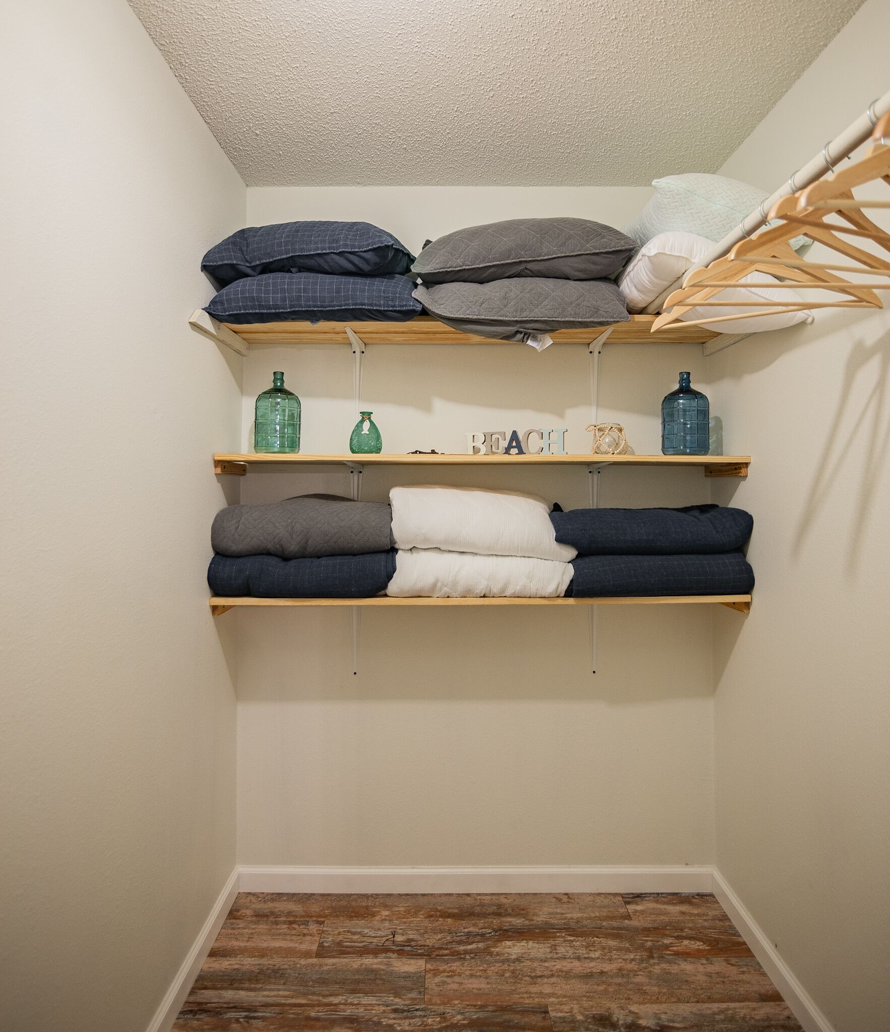 A storage area with shelves holding folded blankets and pillows, a wooden floor, and a hanging rack.