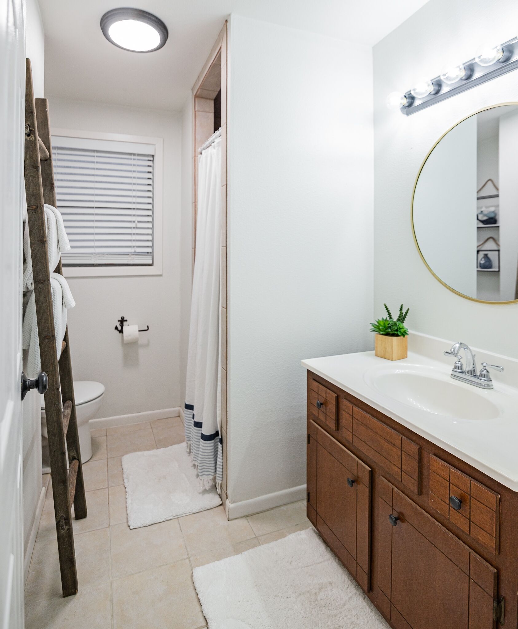 A bathroom with a wooden vanity, a round mirror, a white sink, and a shower area.