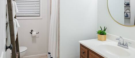 A bathroom with a wooden vanity, a round mirror, a white sink, and a shower area.