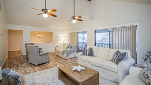 A spacious living room with a high ceiling, two ceiling fans, a large window with blinds, and a view of the outdoors. - Spacious Vacation Home: Sleeps 16, 1/2 mi to Beach & Boat Ramp - Family Friendly (Port O'Connor)
