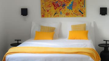 Habitación de hotel con cama, dos almohadas amarillas, una colcha amarilla y un cuadro abstracto de colores en la pared.