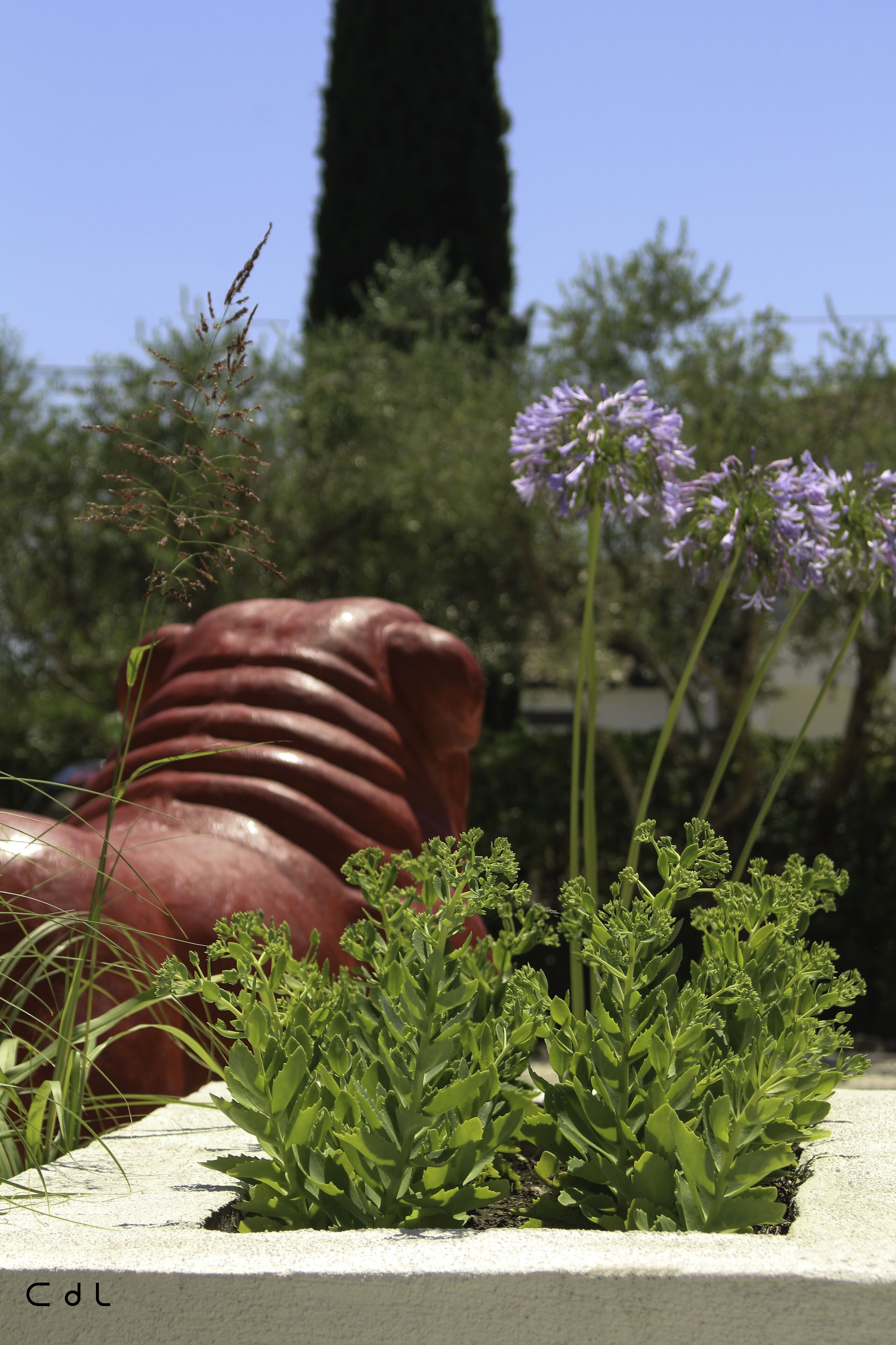 A garden with a concrete planter, green plants, and a large red sculpture.