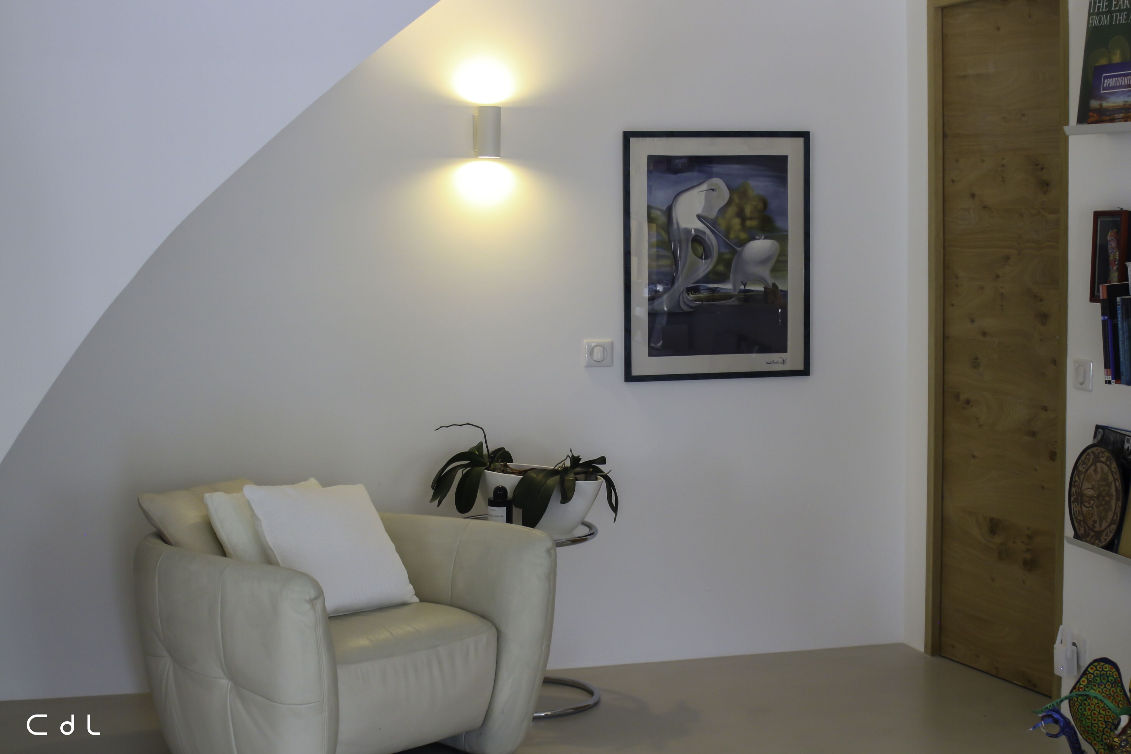 A modern living room with a white leather sofa, a side table with a potted plant, a framed artwork on the wall, and a wooden door.