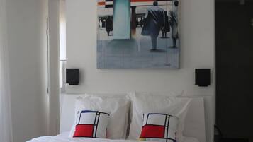 A hotel room with a bed, white pillows, a painting on the wall, and a window.