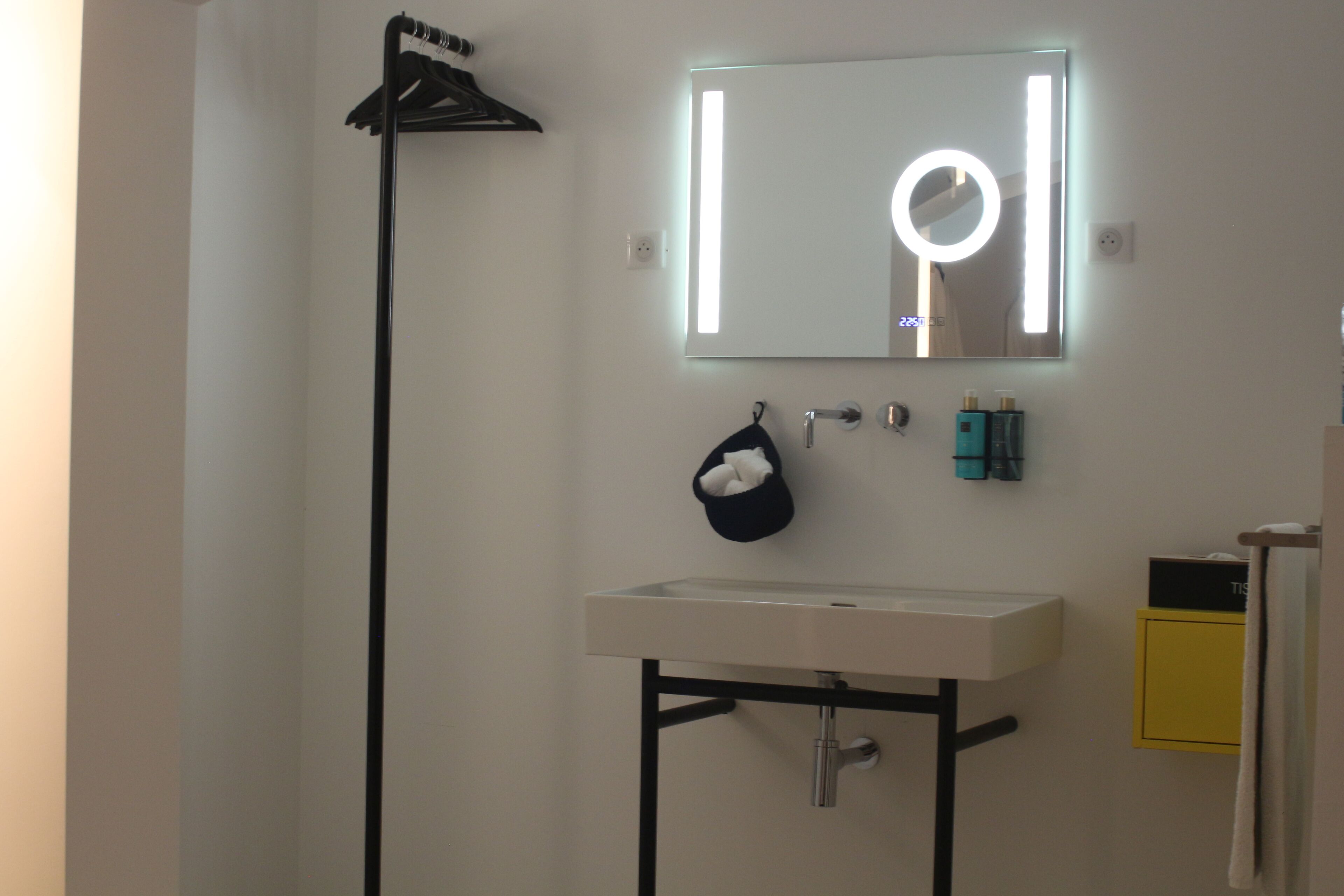 Een badkamer met een wit wastafelmeubel, een spiegel met verlichting, een handdoekrek en toiletartikelen.