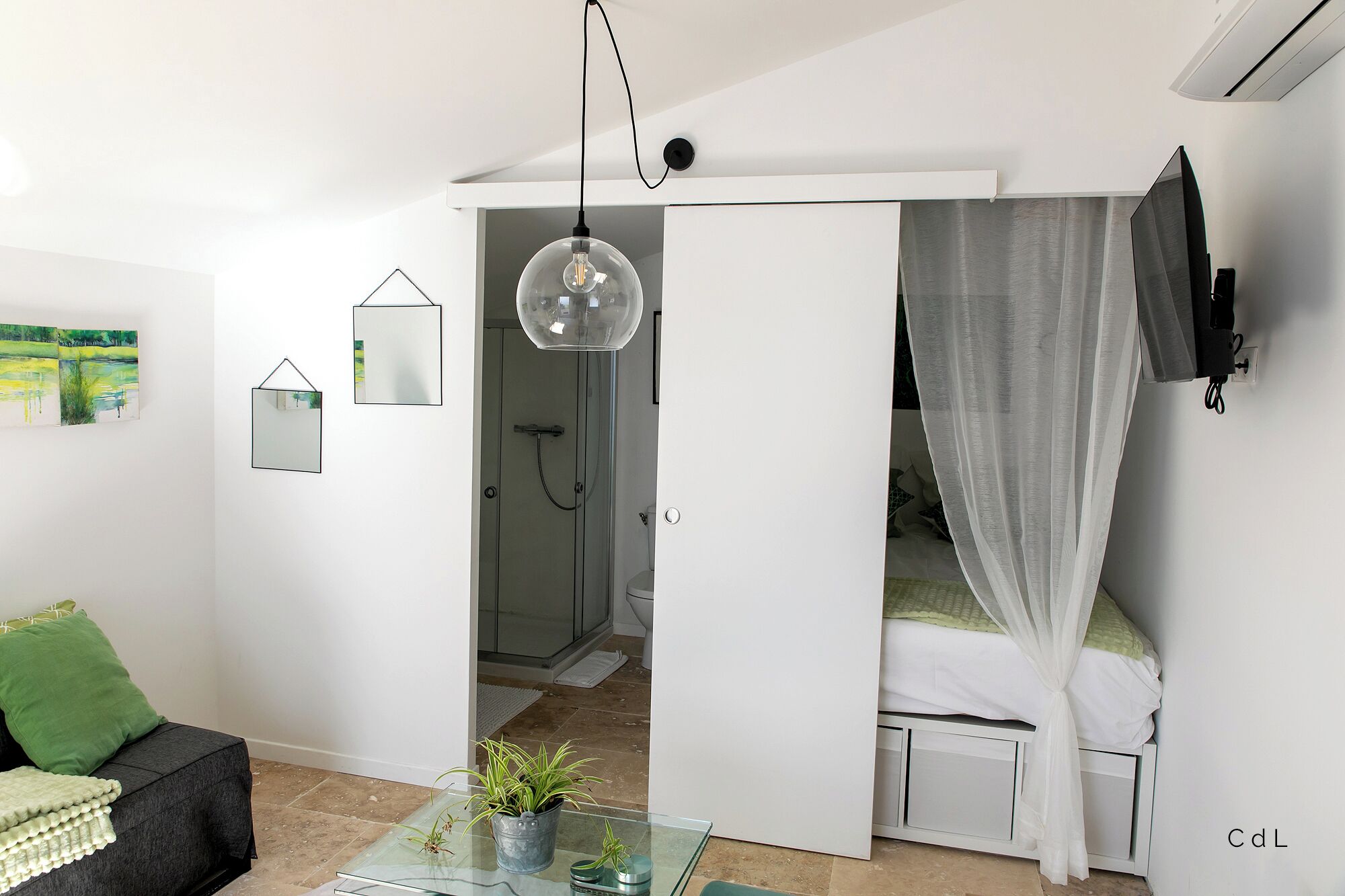 Un dormitorio moderno con una mesa de vidrio, una cama con dosel, ducha y televisor montado en la pared.