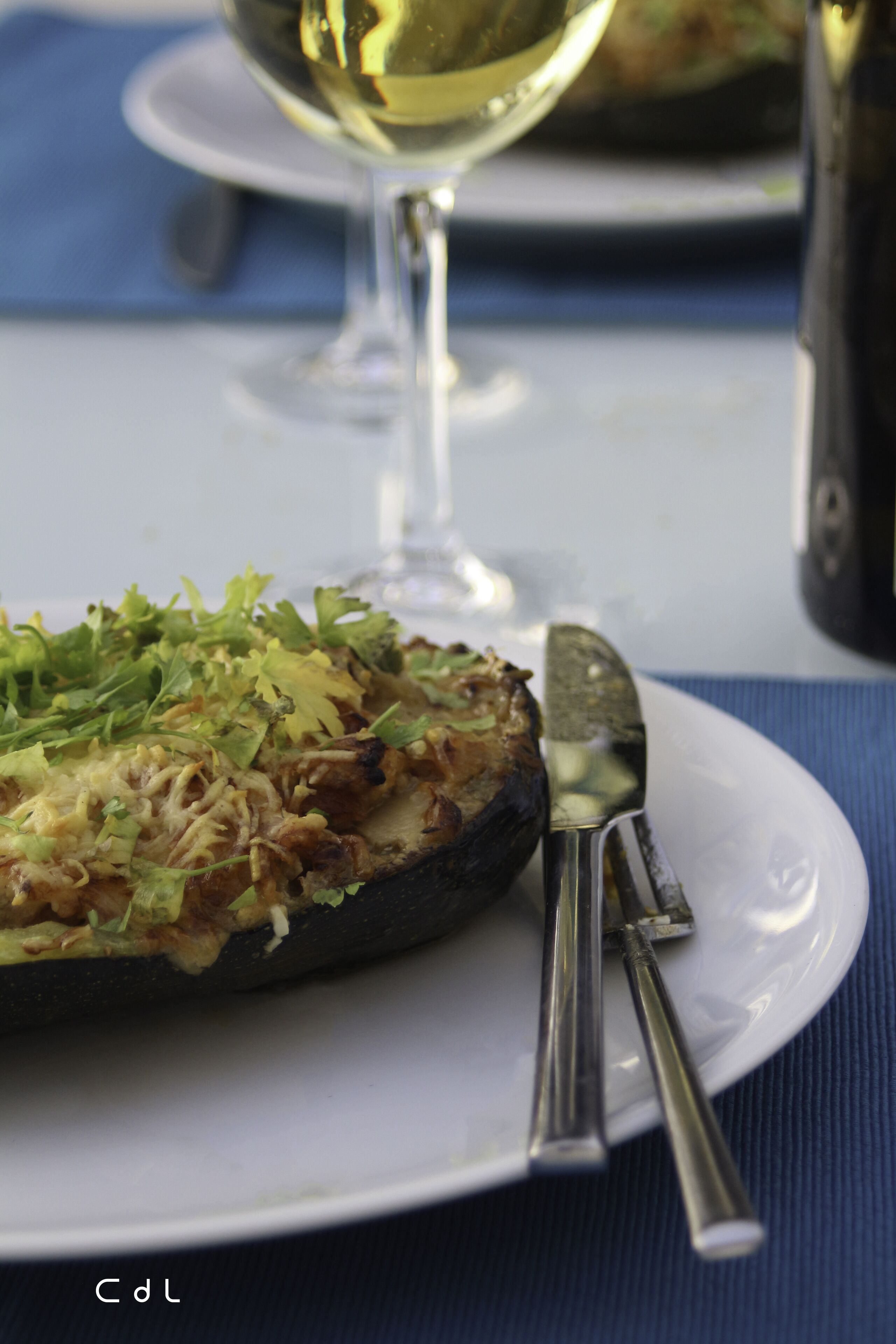 A plate with a stuffed vegetable dish, a glass of white wine, and a knife on a blue tablecloth.