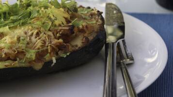 A plate with a stuffed vegetable dish, a glass of white wine, and a knife on a blue tablecloth.
