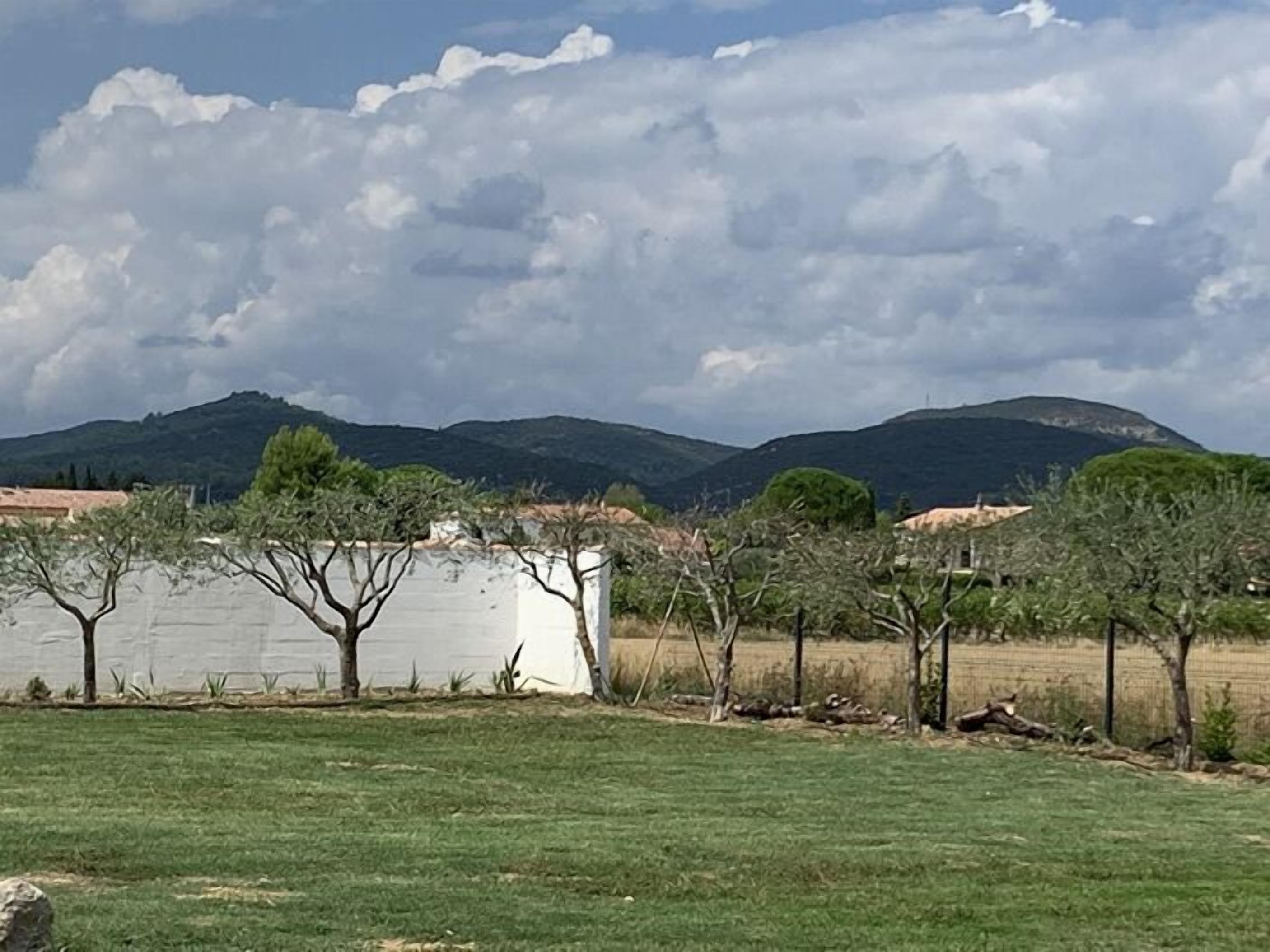 Ein grasbewachsenes Feld mit einem weißen Gebäude, Bäumen und Bergen im Hintergrund.