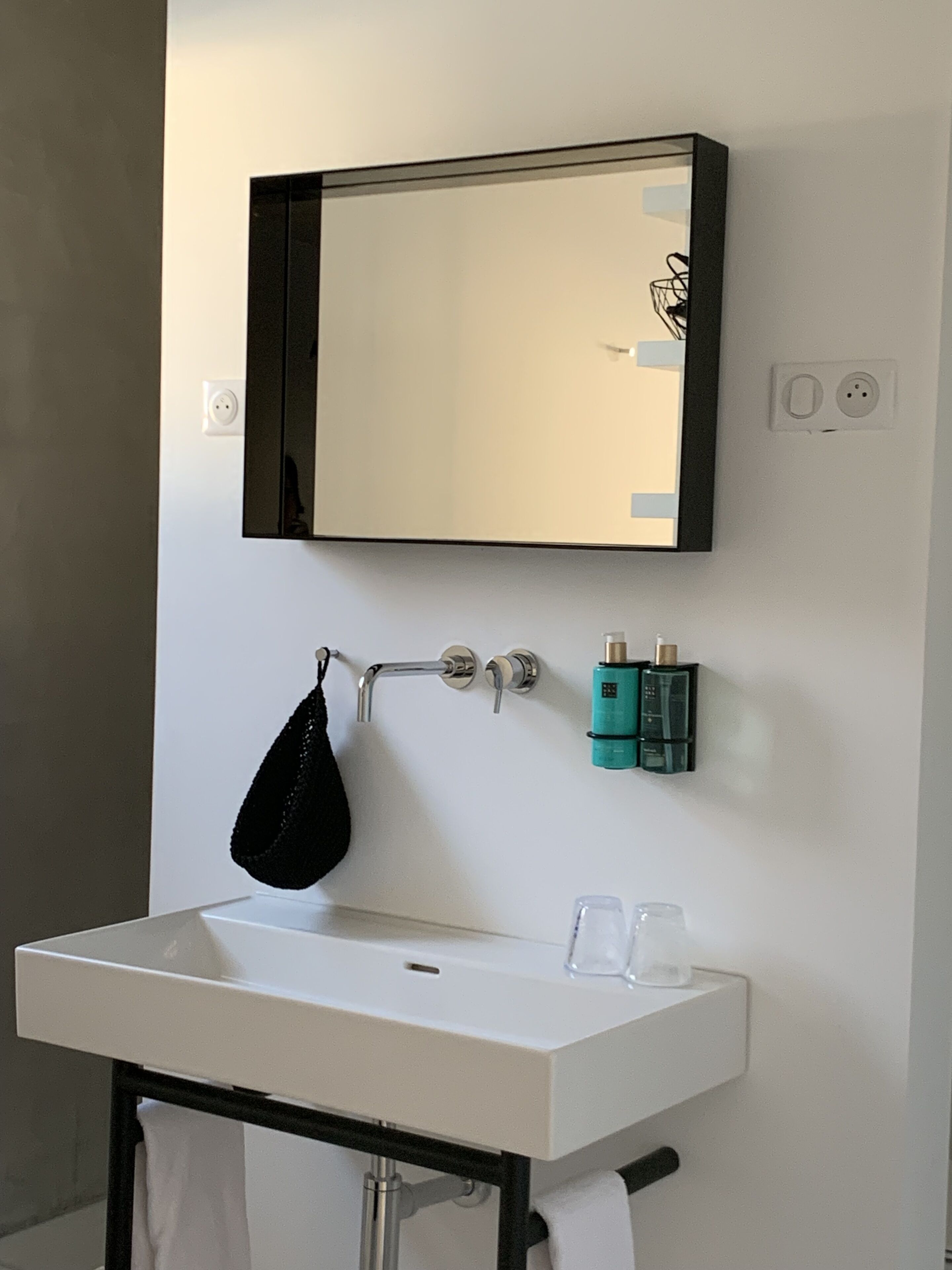Un baño con un lavamanos blanco, un espejo y un perchero para toallas.