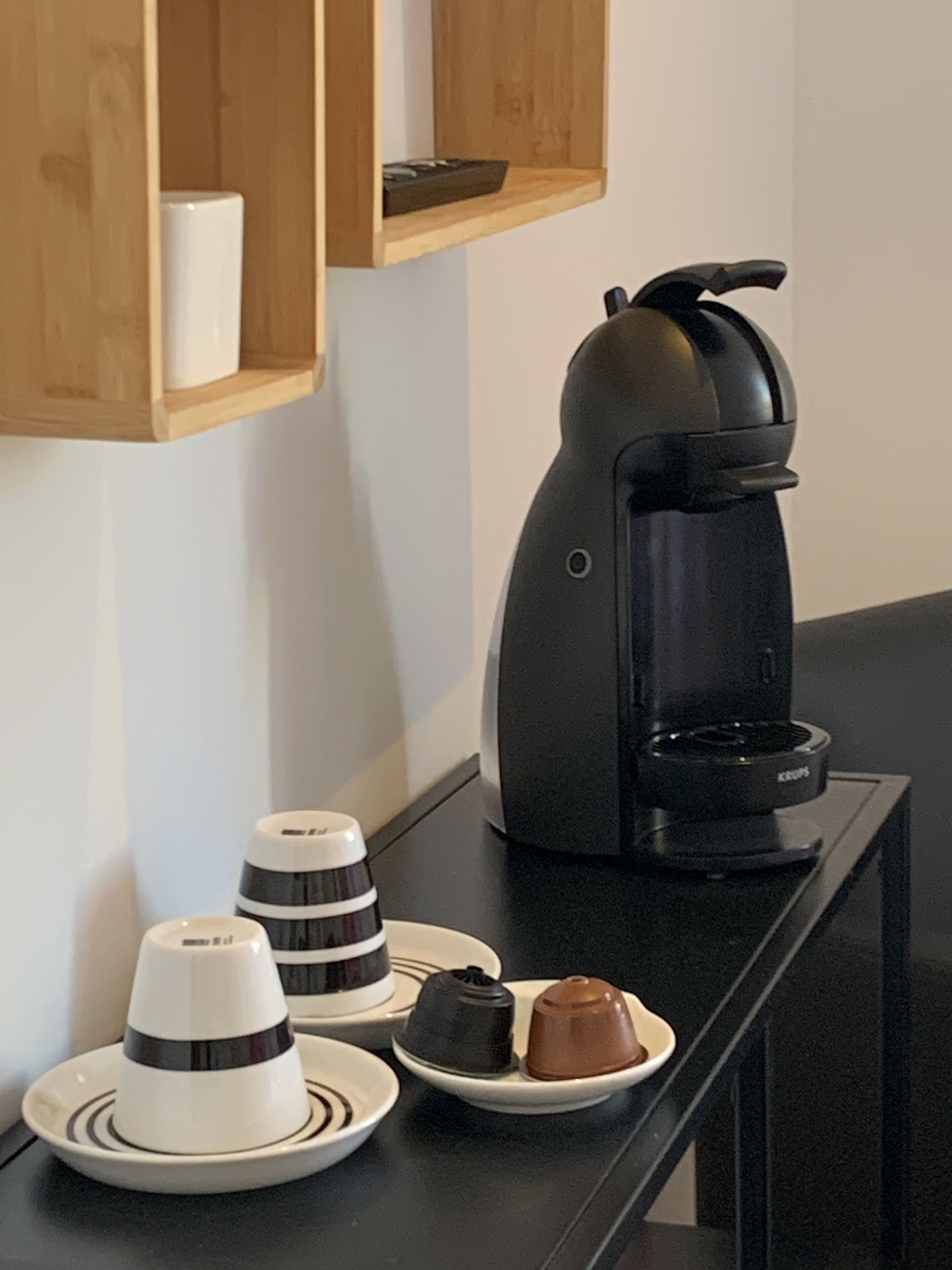 A kitchen counter with a coffee maker, a plate with two cups, and a plate with a dessert.