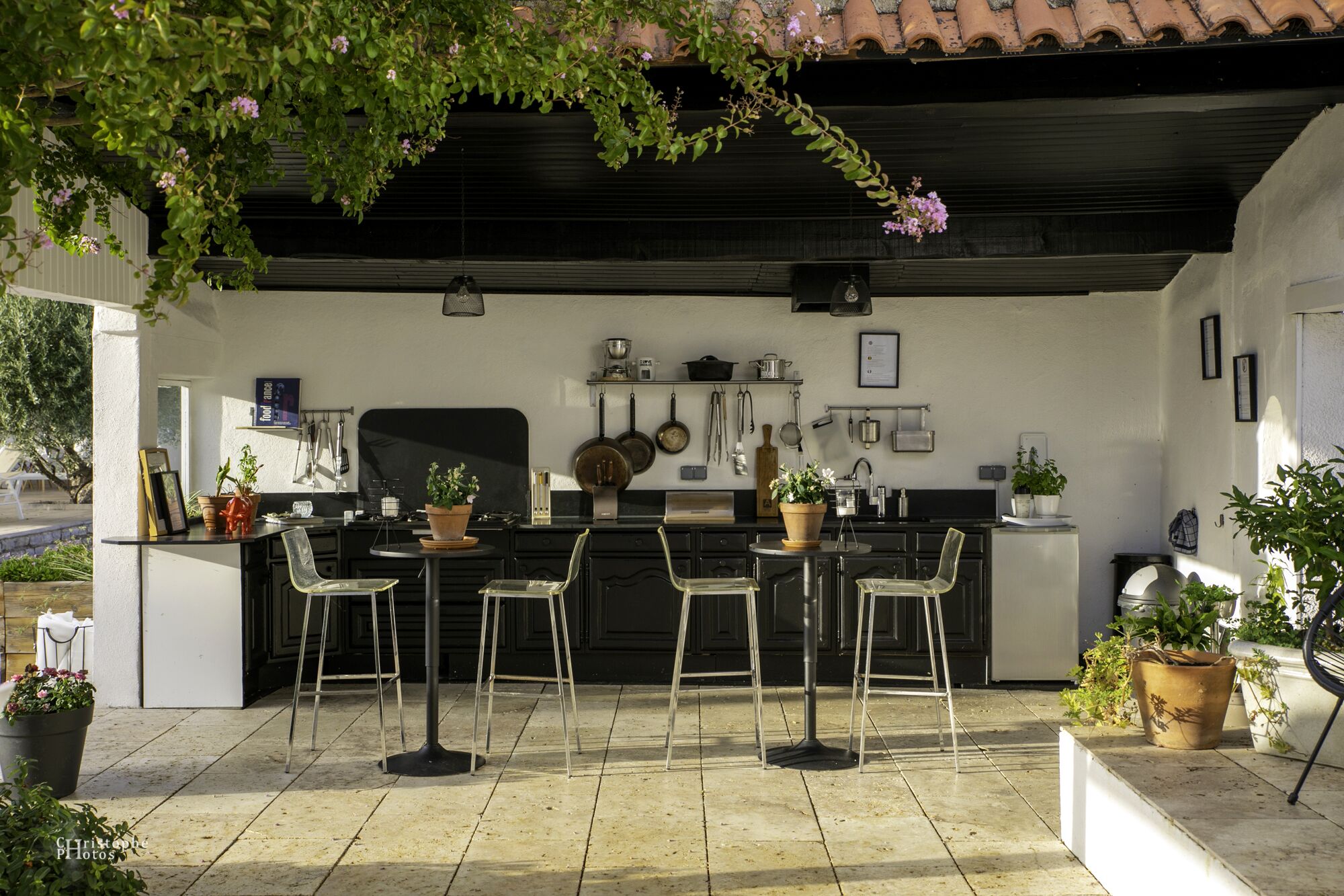 An outdoor kitchen area with a dining set, potted plants, and kitchen utensils on the wall.