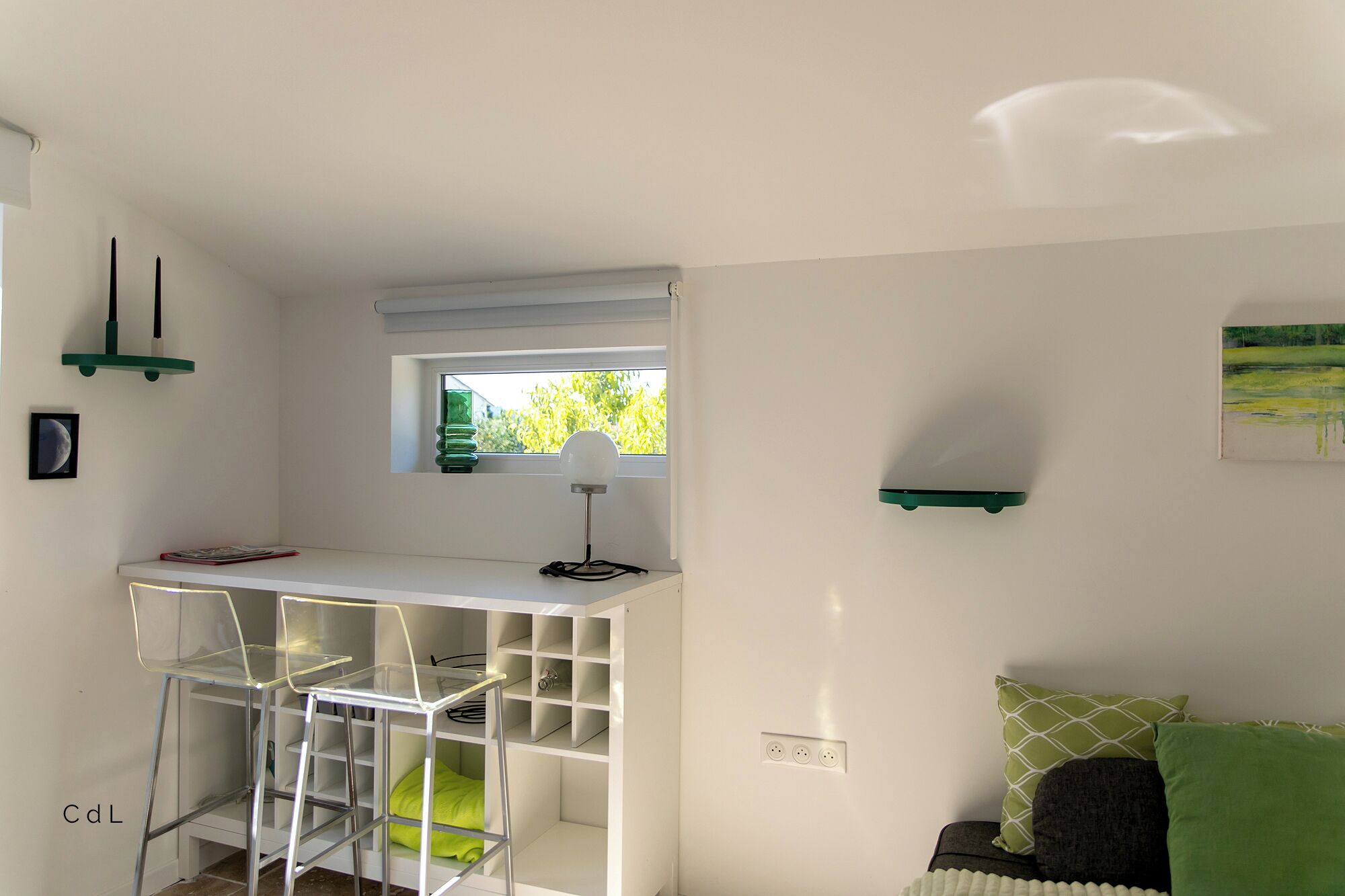Une pièce de taille modeste, avec un bureau blanc, une chaise, une petite fenêtre et un canapé vert.