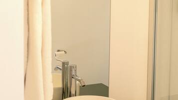 Une salle de bain avec un lavabo rond blanc, un miroir et une douche.