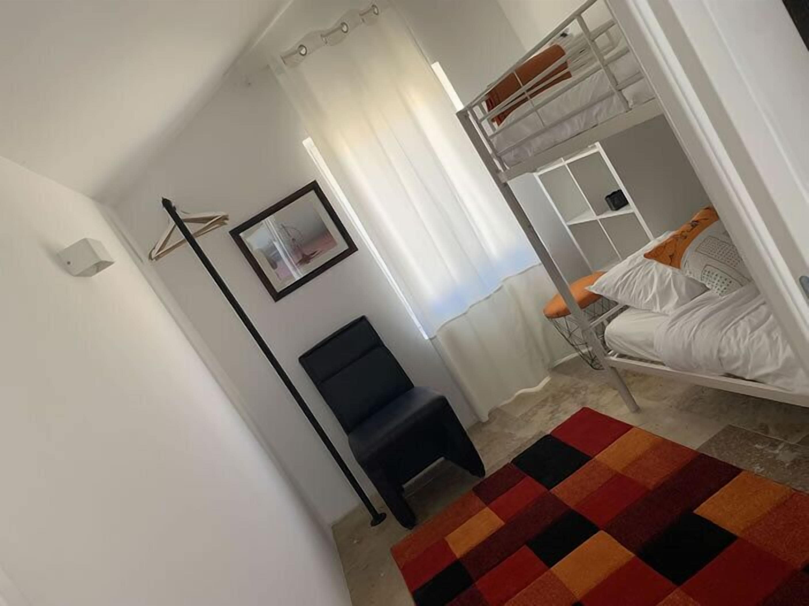 A dorm-style room with bunk beds, a black chair, a colorful rug, and a framed picture on the wall.