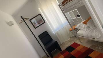 A dorm-style room with bunk beds, a black chair, a colorful rug, and a framed picture on the wall.