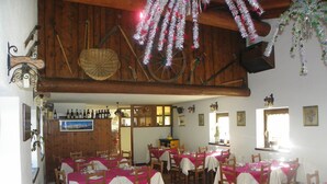 A restaurant with multiple tables covered in pink tablecloths, wooden chairs, and a rustic wooden ceiling. - Hotel Les Granges (La Thuile)