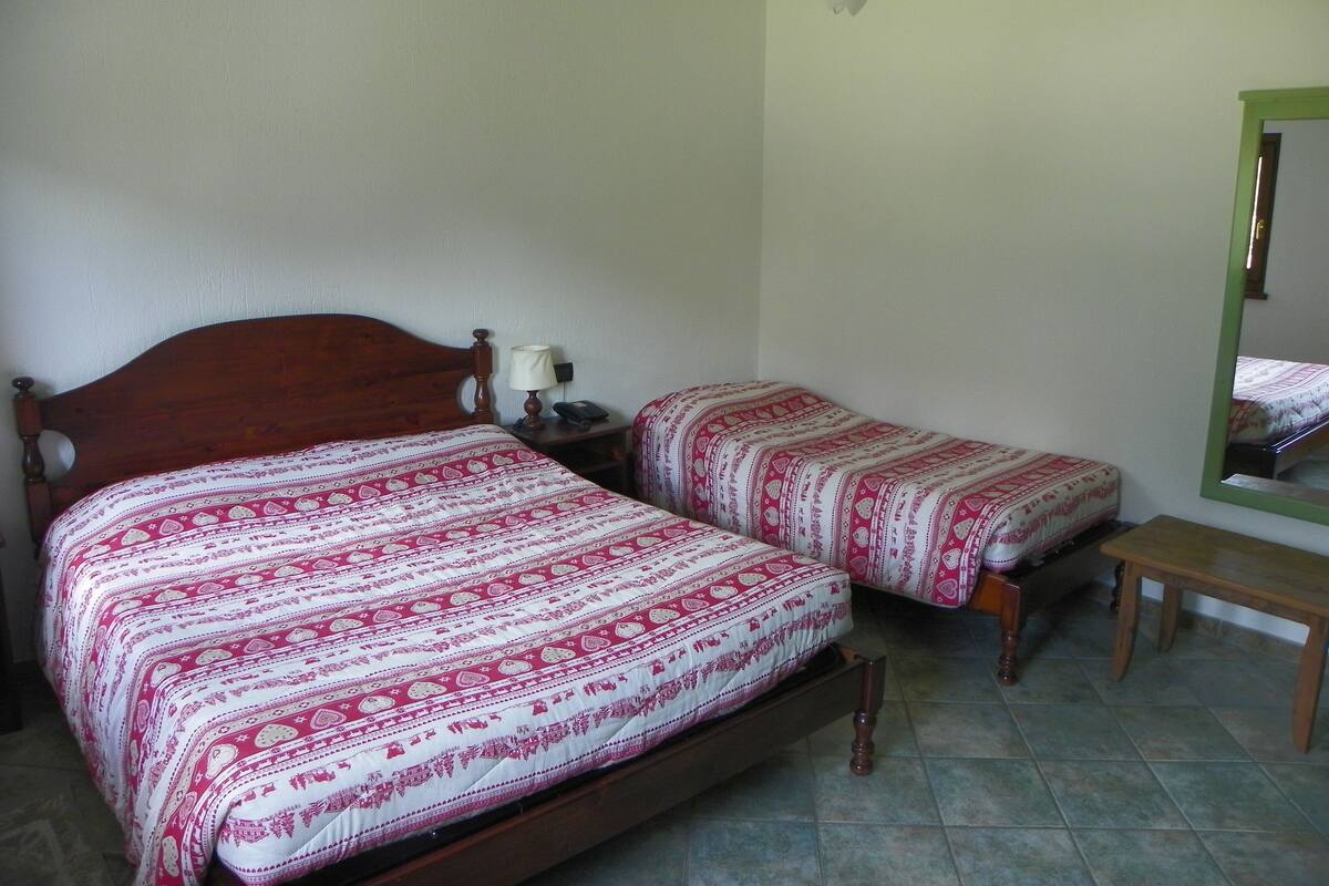 Un dormitorio con dos camas individuales, una mesita de noche con lámpara, una pequeña mesa y un espejo en la pared.