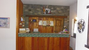 A reception area with a wooden counter, stone wall, and various signs and decorations. - Hotel Les Granges (La Thuile)