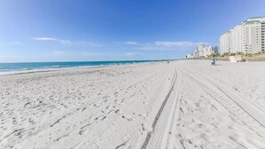 A wide sandy beach with footprints leading to the ocean, a clear blue sky, and high-rise buildings in the background. - Lovely Studio Condo 200 Yards from the Atlantic (Myrtle Beach)