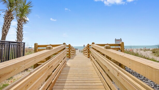 A wooden boardwalk leading to a beach with palm trees and a signboard. - Lovely Studio Condo 200 Yards from the Atlantic (Myrtle Beach)