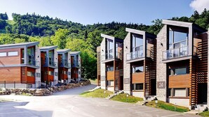 A row of modern multi-story buildings with balconies, set against a backdrop of a forested hillside. - 24-Chalet à Stoneham (Stoneham-et-Tewkesbury)