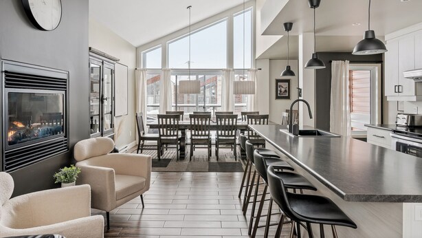 A modern kitchen with a large island, bar stools, and a dining area with a fireplace. - 24-Chalet à Stoneham (Stoneham-et-Tewkesbury)