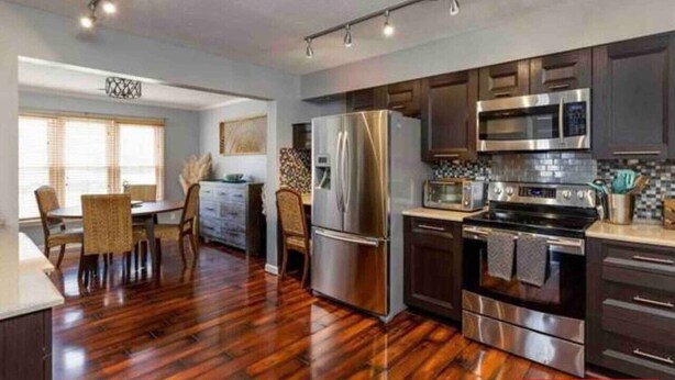 A modern kitchen with stainless steel appliances, a dining area with a wooden table and chairs, and a large window providing natural light.