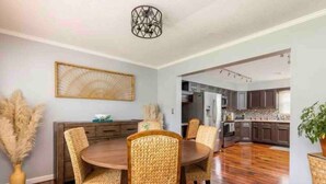 A dining area with a round table and wicker chairs, a decorative wall piece, and a vase with pampas grass.