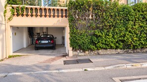 A car parked inside a garage attached to a building with a stone wall and greenery.
