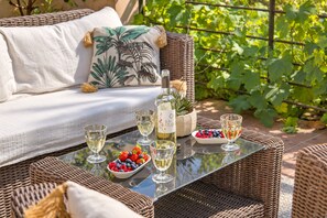 A wicker outdoor seating area with a bottle of white wine, glasses, and a bowl of mixed berries.