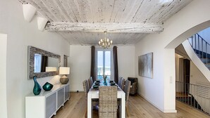 Un coin repas avec une table blanche, des chaises en osier, un lustre et une vue par la fenêtre.