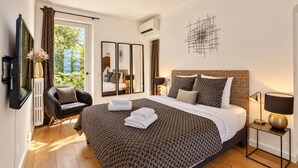 A hotel room with a large bed, a sitting area with a chair, a TV, and a view of greenery outside. - ☀️La plage☀️<br>Classified ⭐️⭐️⭐️⭐️ (Antibes)