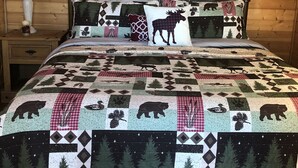 Ein gemütliches Zimmer mit Holzbalkendecke, einem Bett mit einem Zudecke mit Tiermotiven, einem Nachttisch mit Lampe und einem Fenster mit Vorhängen.