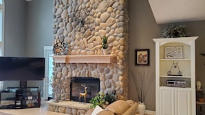 A living room with a stone fireplace, a flat-screen TV, a sofa, and a cabinet with decorative items. - Lakefront Sunsets and Sandy Beach in Rockford, MI (ROCKFORD)