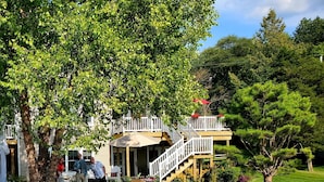 A lakeside property with a wooden deck, outdoor seating, and a stone pathway leading to a dock. - Lakefront Sunsets and Sandy Beach in Rockford, MI (ROCKFORD)