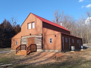 A wooden barn with a red roof, a wooden staircase, and a small porch.