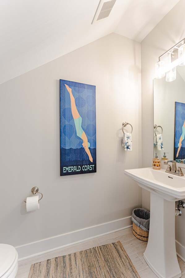 A bathroom with a white sink, a mirror, a towel rack, a toilet, and a framed artwork on the wall. - Sol Mate-5/3.5 Community Pool/Pickleball. Steps to beach walkover!-SPECIALS (Port St Joe)