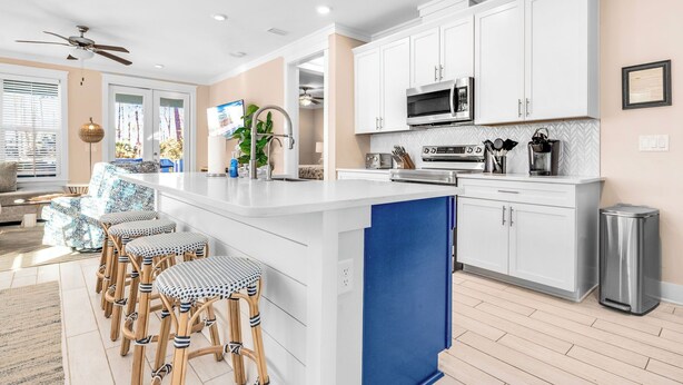 Een moderne keuken met witte kasten, een blauwe accentmuur en een bar met barkrukken.