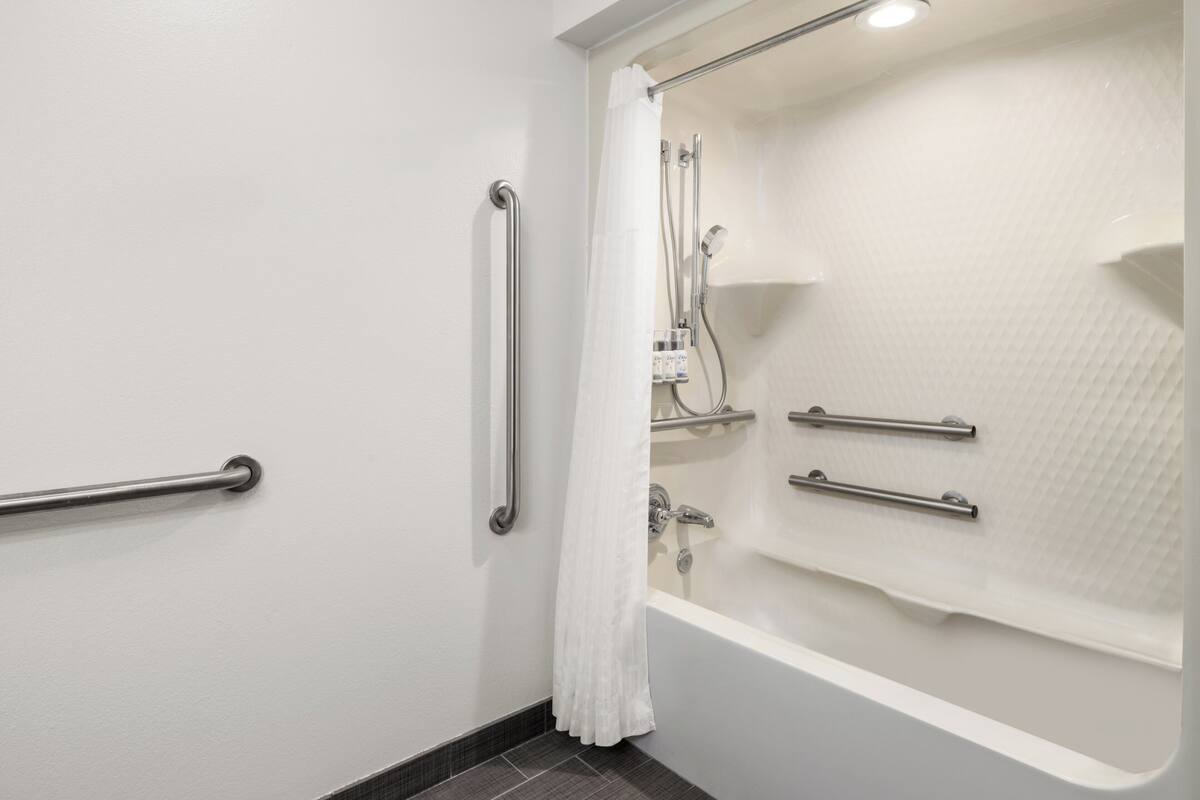 A bathroom with a bathtub, a shower, and a toilet. There are grab bars installed for safety.