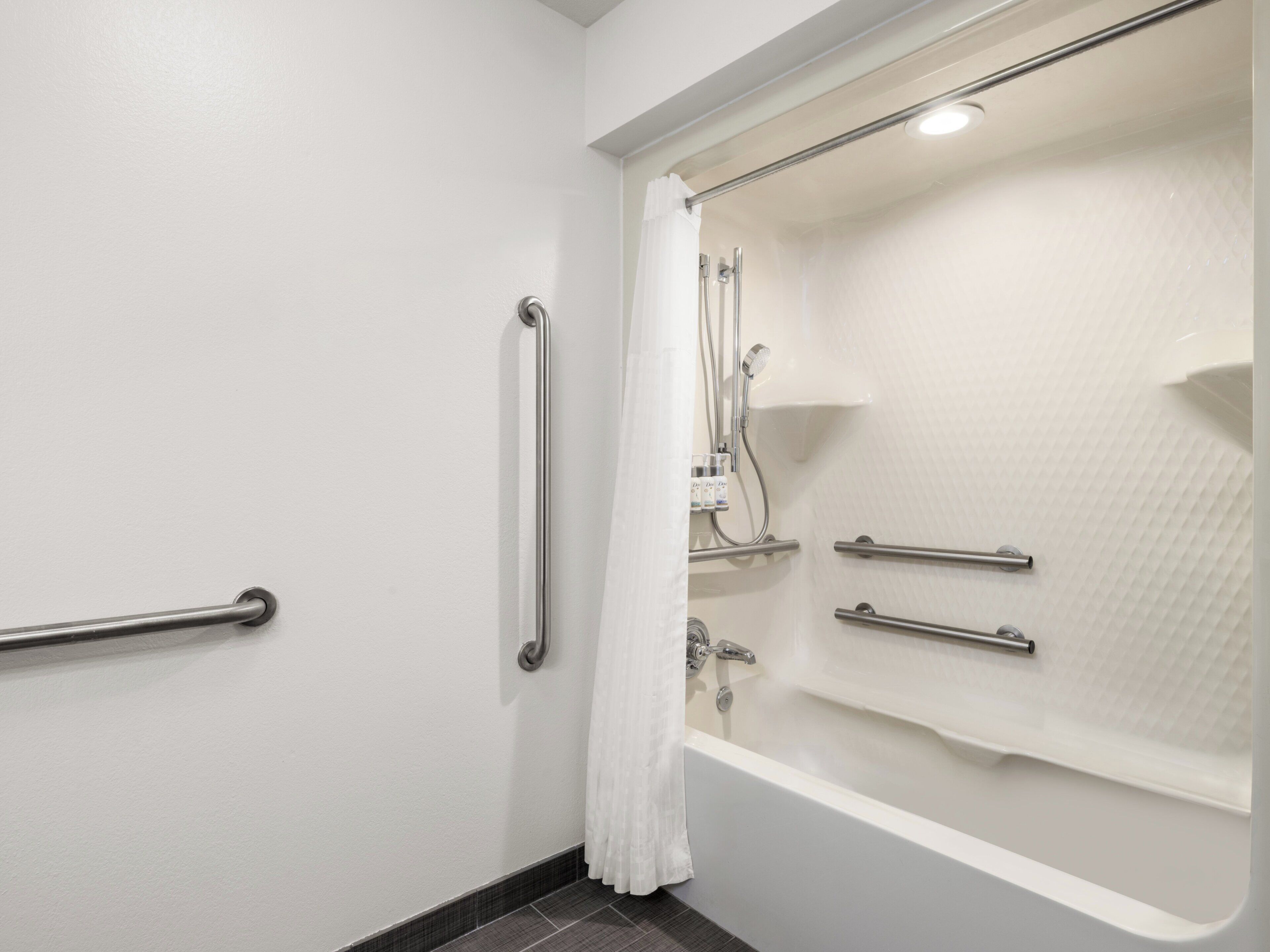 A bathroom with a bathtub, a shower, and a toilet. There are grab bars installed for safety.