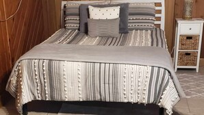 Een bed met gestreepte lakens, een hoofdbord en een nachtkastje met een lamp.