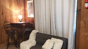 Een gezellige kamer met een donkere bank, twee stoelen, een klein rond tafeltje en een houten wand.