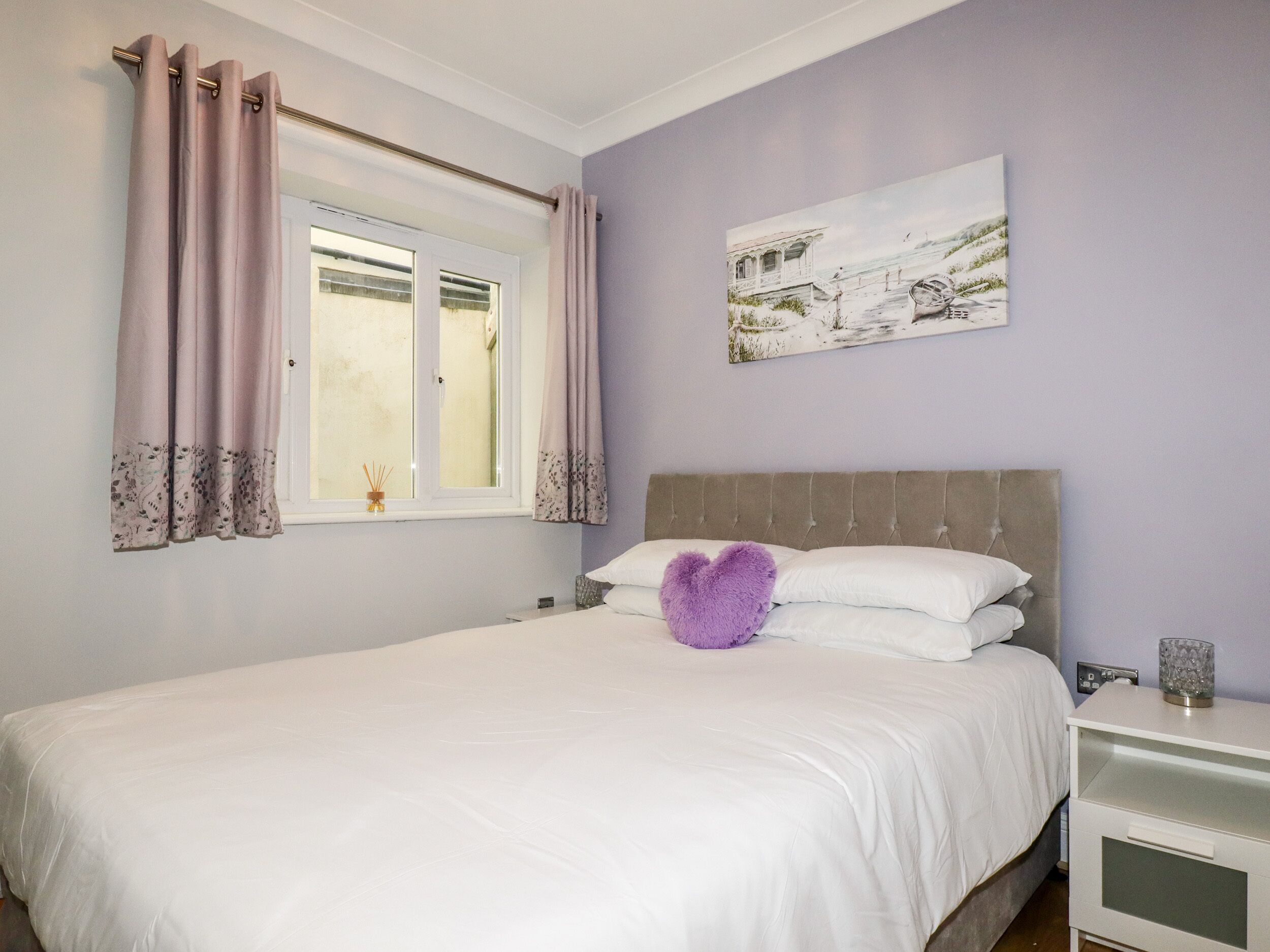 A bedroom with a bed, a nightstand, a window with curtains, and a painting on the wall.