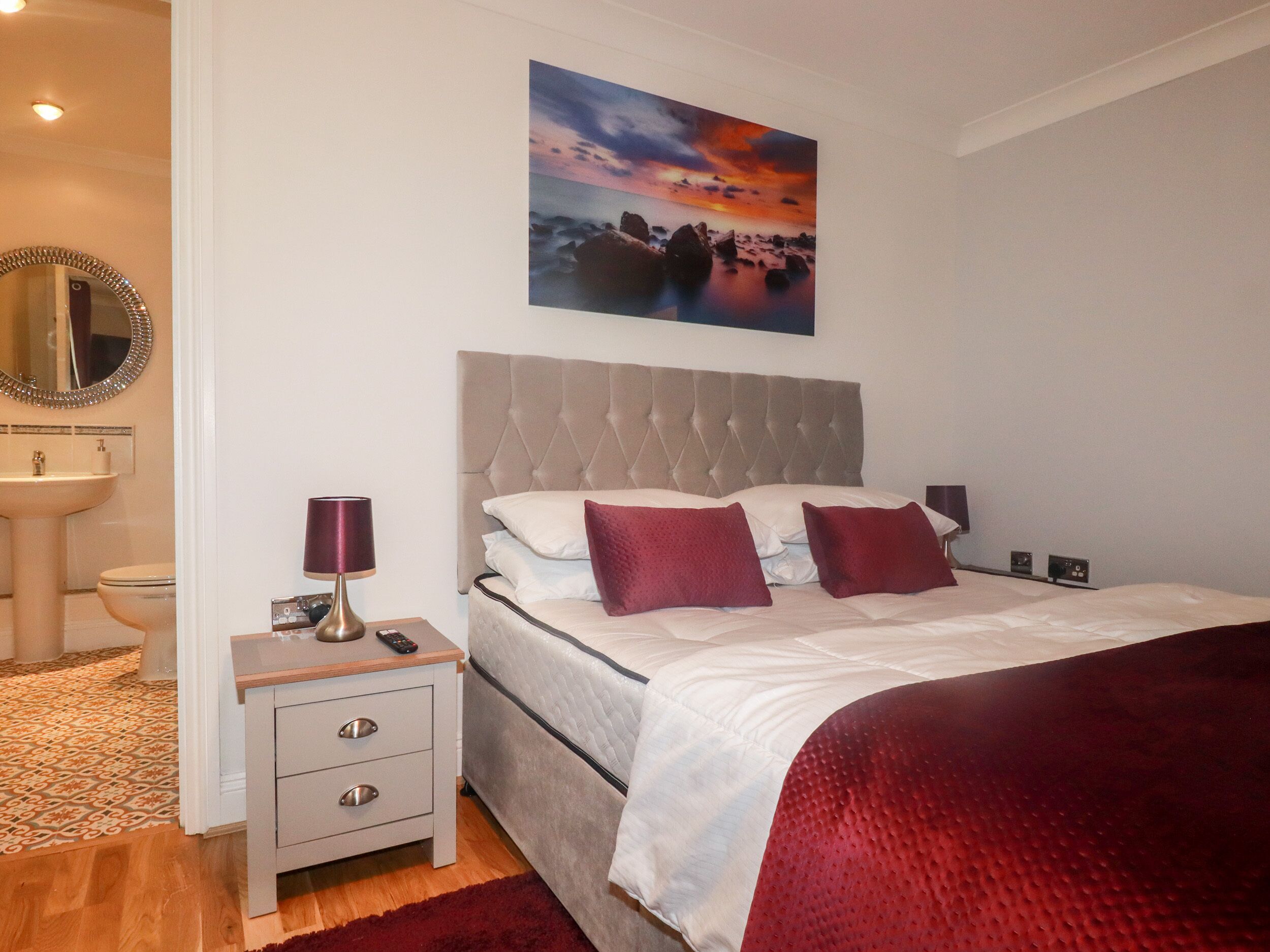 A bedroom with a bed, bedside tables, a nightstand, a mirror, and a painting on the wall.