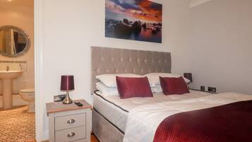 A bedroom with a bed, bedside tables, a nightstand, a mirror, and a painting on the wall.