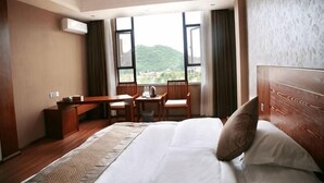 A hotel room with a large bed, a desk, and a chair, with a view of greenery outside. - Longhuyuan Hostel (Yanshan)